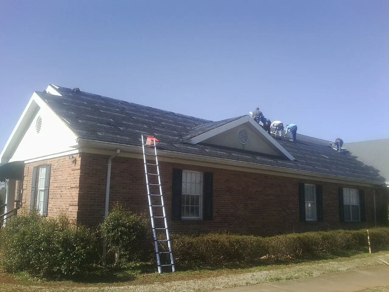 Crew tearing shingles off a brick ranch roof with a ladder set — Metal Roof Repair work by our crew in Magnolia