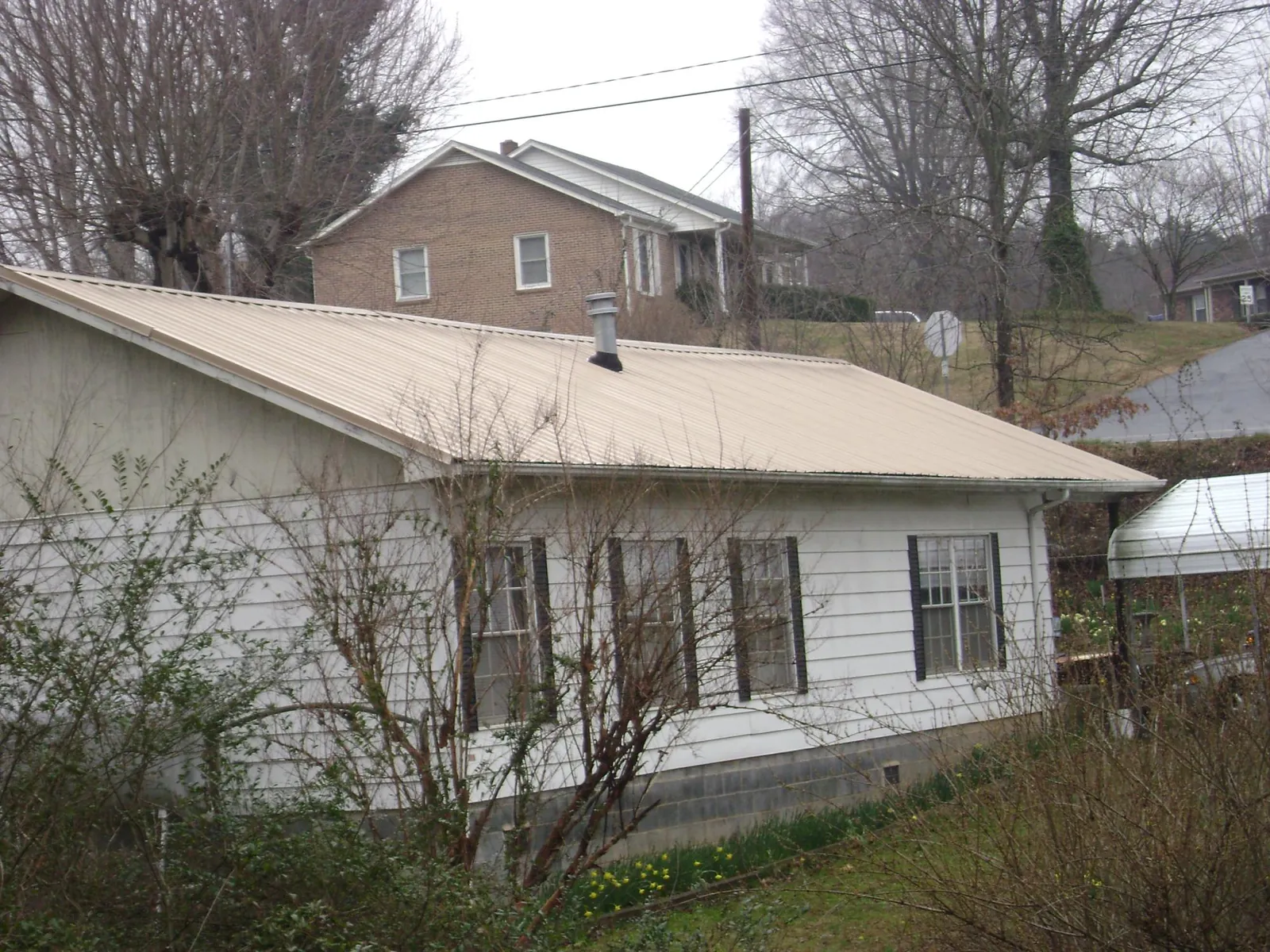 Tan metal roof on a white sided house set into a hillside — Commercial Roofing by Roofing Brothers in Magnolia